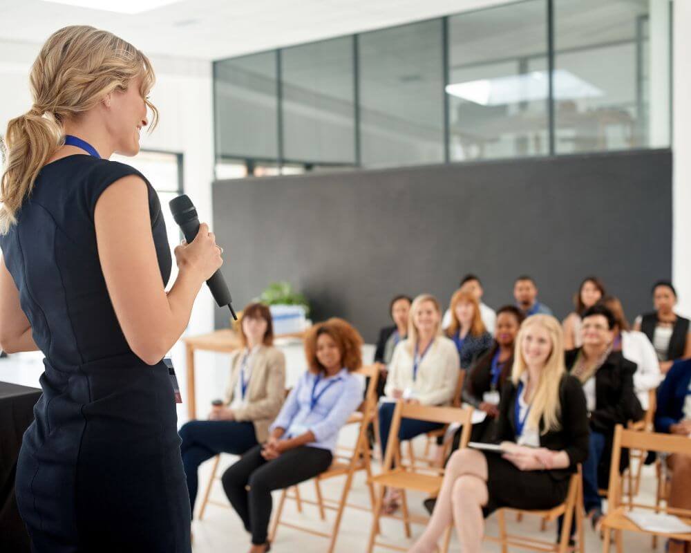 35 profiel toont oplossingen vinden en leiderschap tonen Een vrouw die een toespraak geeft aan een zaal vol bedrijfspersoneel