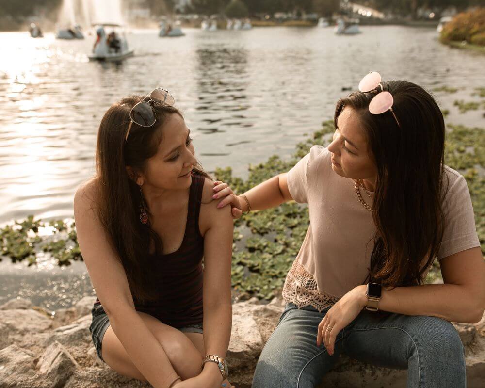 Een vrouw en haar vriendin praten aan de rivier, beiden ontspannen en glimlachend.