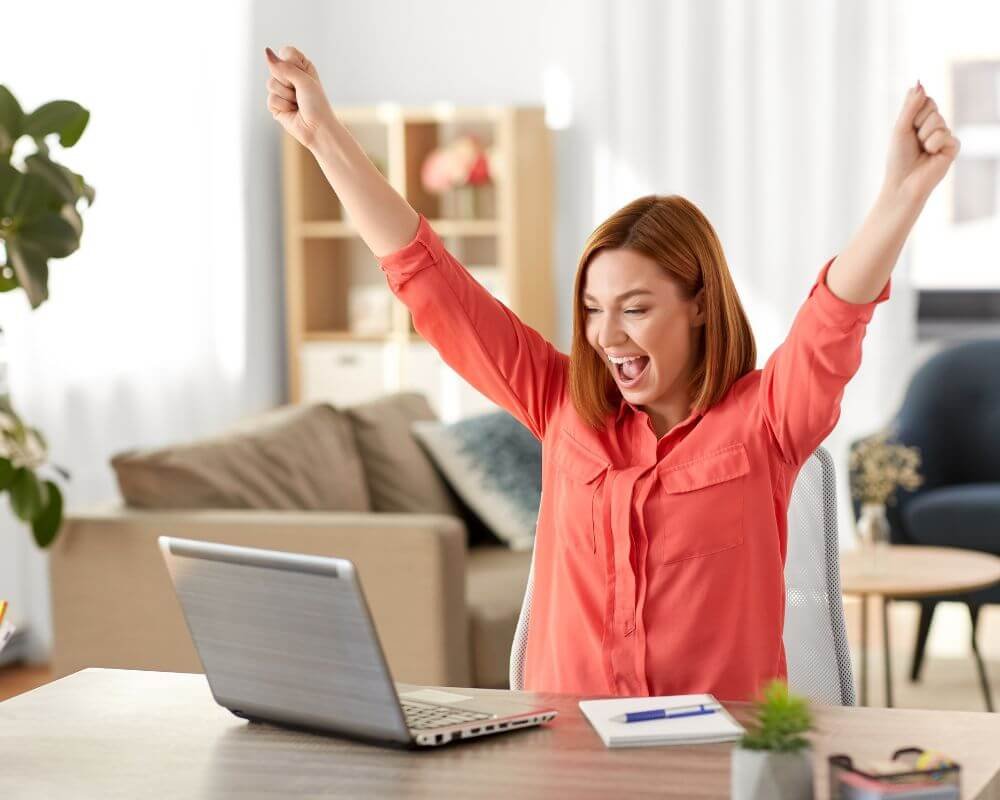 Generatoren zijn de bouwers van de samenleving Een vrouw die haar armen omhoog steekt terwijl ze aan haar bureau voor haar laptop zit